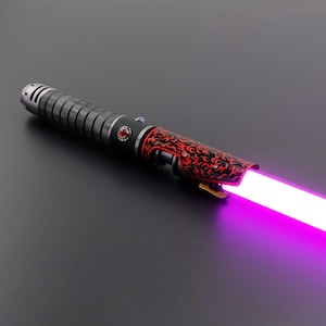 May include: A lightsaber with a black and red hilt and a purple blade. The hilt has a textured grip and red decorative elements. The blade glows brightly, emitting a purple light.