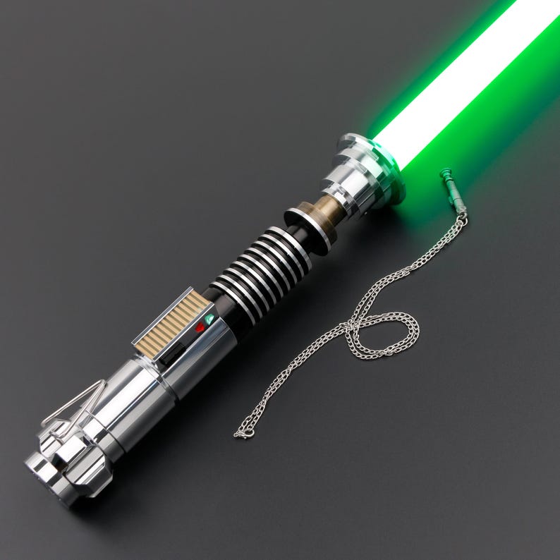 May include: A silver and black lightsaber with a green blade and a silver chain attached to the hilt.