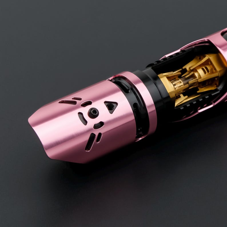 May include: Close-up of a pink and gold lightsaber hilt. The hilt features a cat-shaped design with cut-out details. The internal components are visible, showcasing gold-colored mechanical parts. The lightsaber has a sleek, modern design.