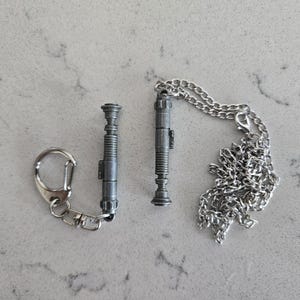 May include: Two silver lightsaber keychains, one on a silver chain and the other on a silver key ring.