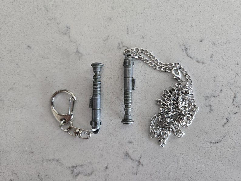 May include: Two silver lightsaber keychains, one on a silver chain and the other on a silver key ring.