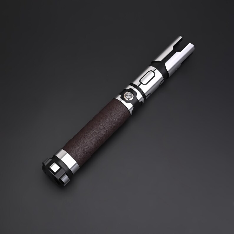 May include: A lightsaber with a brown leather grip, silver accents, and a black button. The blade emitter is silver with a split design. The hilt has a series of silver bands. The lightsaber is a prop or collectible.
