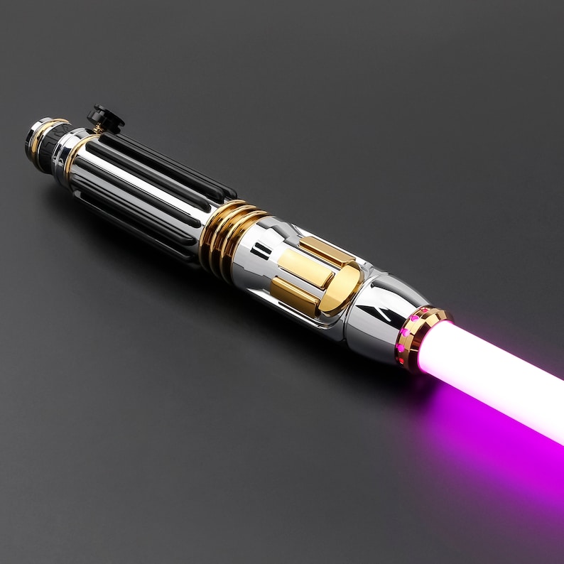 May include: A black and silver lightsaber with gold accents and a pink blade. The lightsaber has a black handle with a silver blade and a gold ring around the blade.