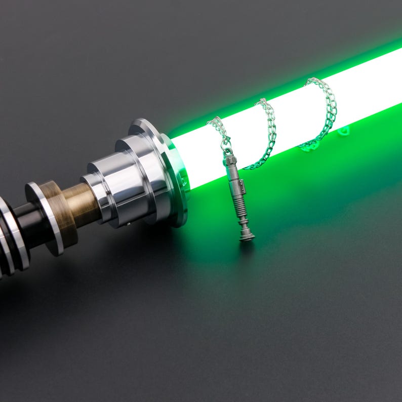May include: A silver lightsaber hilt with a green blade and a silver lightsaber charm hanging from a chain.