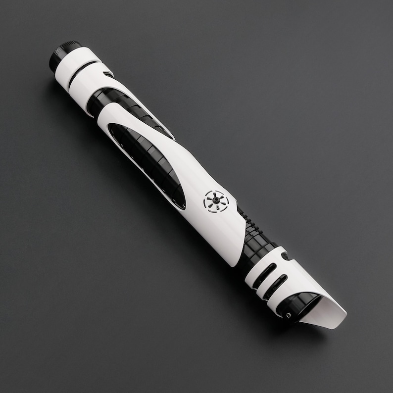 May include: A white and black lightsaber prop with a detailed design. The hilt features a combination of white and black panels, with a circular emblem. The lightsaber has a futuristic aesthetic and is set against a dark background.