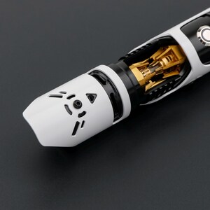 May include: A close-up of a white and black lightsaber with gold accents. The lightsaber has a detailed design with a white hilt and a black section. The blade emitter features a series of cut-out shapes. The overall design is futuristic and sleek.