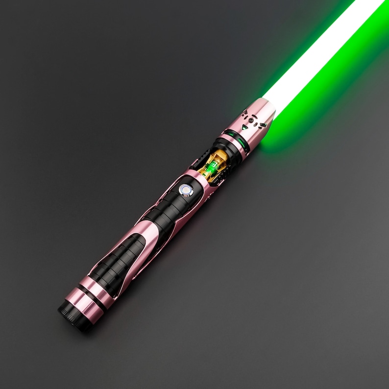May include: A rose-gold and black lightsaber with a bright green blade. The hilt features intricate detailing, including a black grip section and a gold-colored internal component. The blade emits a vibrant green glow against a dark background.