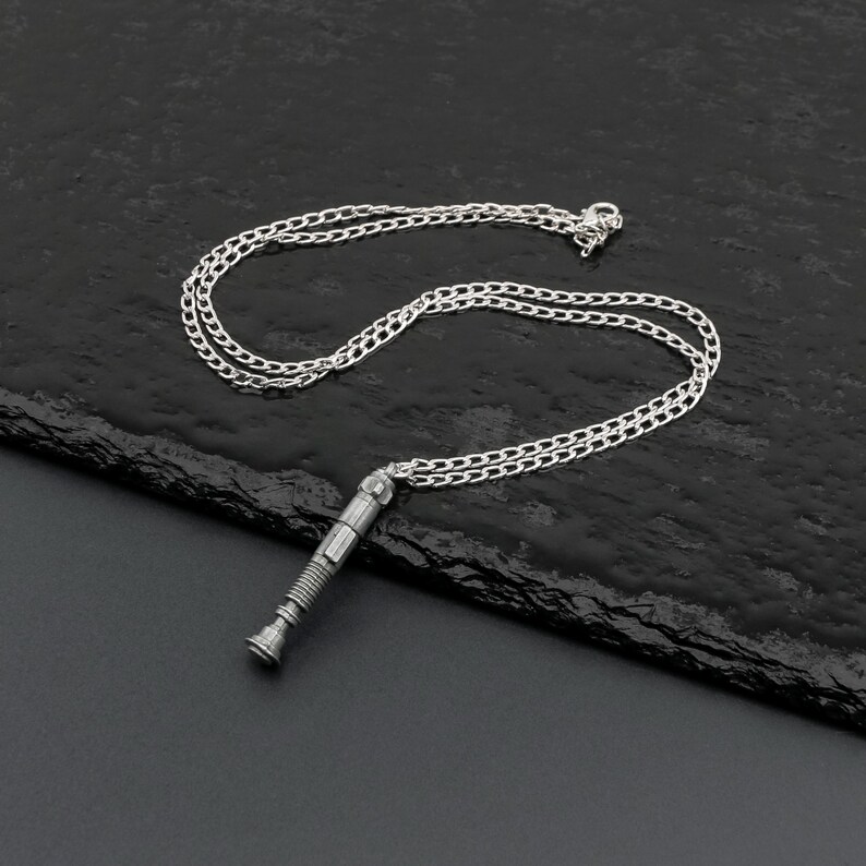 May include: A silver necklace with a detailed, cylindrical pendant that resembles a futuristic weapon. The chain is a classic, linked style.