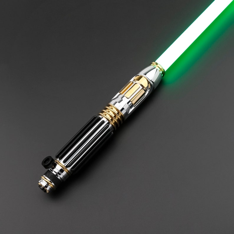 May include: A silver and gold lightsaber with a green blade. The lightsaber has a black grip and a gold accent near the blade.