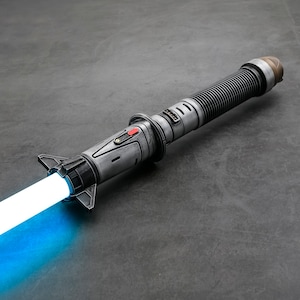 Puede incluir: Un sable de luz azul con un mango gris y plateado. El sable de luz est&aacute; encendido y tiene una hoja azul.