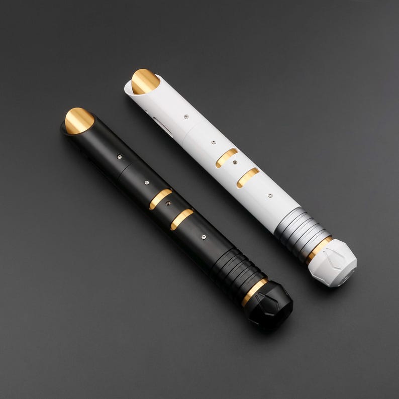 May include: Two futuristic lightsabers, one black and one white, with gold and silver accents. The black saber has a textured grip and a faceted end. The white saber has a silver section near the end and a white tip.
