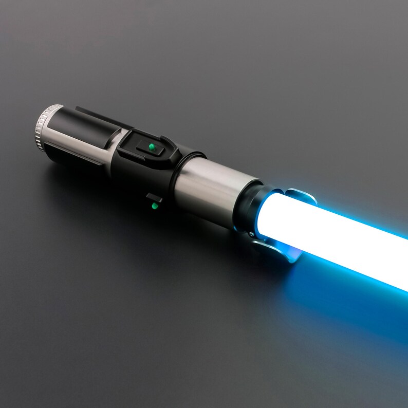 May include: A futuristic lightsaber with a glowing blue blade. The hilt is a combination of black and silver metal, featuring buttons and a textured grip. The blade emits a bright, consistent light.
