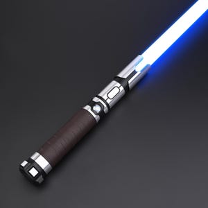 May include: A futuristic lightsaber with a bright blue blade. The hilt has a brown leather grip, silver accents, and black details. The lightsaber is angled diagonally against a dark background.