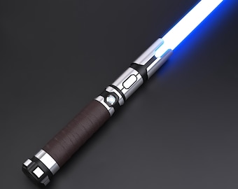 May include: A futuristic lightsaber with a bright blue blade. The hilt features a brown leather grip, silver accents, and black details. The lightsaber is angled diagonally against a dark background.