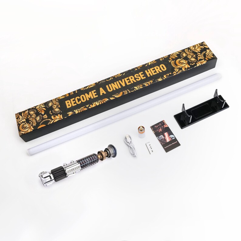 Puede incluir: Un kit de sable de luz con una empu&ntilde;adura plateada y negra, una larga hoja blanca y una caja negra con dise&ntilde;os florales dorados. La caja dice "BECOME A UNIVERSE HERO". Incluye un cable de carga, soporte e instrucciones.