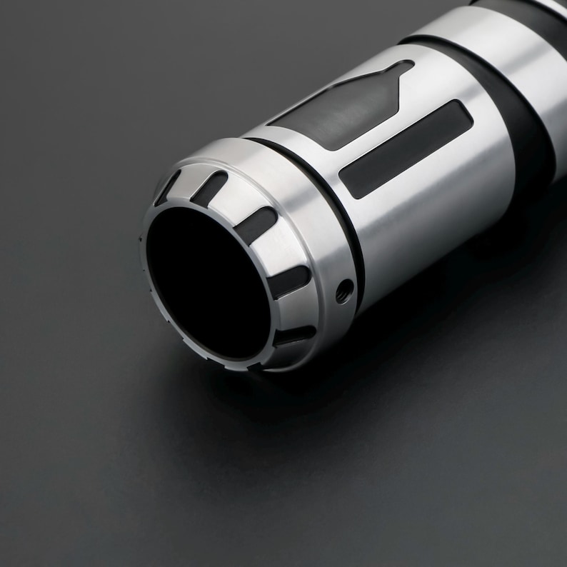 K&ouml;nnte beinhalten: Ein zylindrisches Metallobjekt mit geb&uuml;rstetem Silber-Finish und schwarzen Akzenten. Das Ende weist einen gekerbten, zahnradartigen Rand auf. Der K&ouml;rper zeigt eine ausgeschnittene Flaschensilhouette und einen rechteckigen Schlitz.