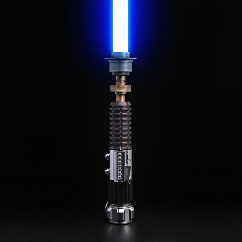 Puede incluir: Un sable de luz azul con una hoja brillante y resplandeciente. El mango es una combinaci&oacute;n de metal plateado, negro y bronce, con detalles intrincados. El sable de luz est&aacute; sobre un fondo negro.