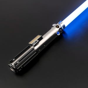 May include: A silver and black lightsaber with a bright blue blade. The hilt features detailed metallic components, including buttons and a rectangular section. The glowing blue blade extends diagonally across a dark background.