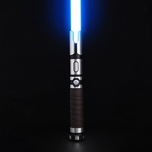 May include: A blue-bladed lightsaber with a silver and black hilt. The hilt has a brown, textured grip and a circular button. The blade glows brightly against a black background. The lightsaber is a prop or toy.