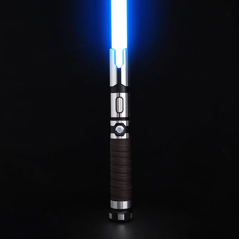 May include: A blue-bladed lightsaber with a silver and black hilt. The hilt has a brown, textured grip and a circular button. The blade glows brightly against a black background. The lightsaber is a prop or toy.