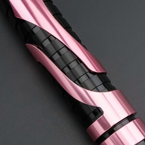 May include: Close-up of a black and pink object with a sleek, modern design. The object features a series of black, cylindrical segments encased in curved, metallic pink panels. The color scheme creates a striking contrast, highlighting the object's form.