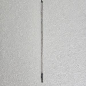 May include: A silver chain necklace with a small, black, cylindrical pendant hanging from it.