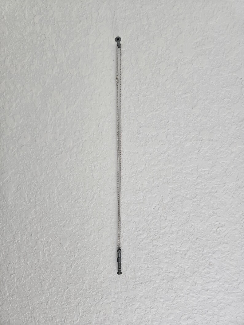 May include: A silver chain necklace with a small, black, cylindrical pendant hanging from it.