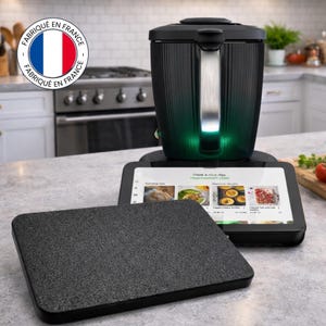Puede incluir: Un electrodoméstico de cocina negro con una pantalla digital, una superficie texturizada y un asa. La pantalla muestra imágenes de comida. Una tabla de cortar negra separada está en primer plano. El aparato tiene una luz verde.