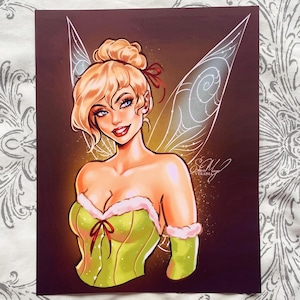 Op de afbeelding: Een digitale illustratie van Tinkerbell, een fee met blond haar en groene vleugels, die een groene en witte jurk draagt met een rode strik. De achtergrond is donkerbruin met gouden glitter.