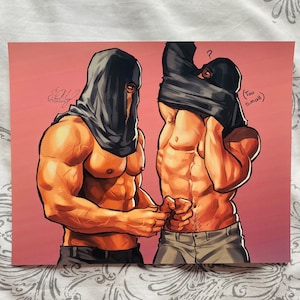 Op de afbeelding: Twee mannen, een met een zwarte kap en de ander met een zwart shirt, staan voor een roze achtergrond. De man met het zwarte shirt trekt zijn shirt uit en onthult zijn gespierde torso. De man met de kap kijkt de man met het zwarte shirt met een vragende blik aan. De tekst "(Te klein)" staat in de rechterbovenhoek van de afbeelding.