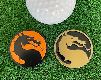 May include: Two golf ball markers with a black dragon design. One marker has an orange background and the other has a gold background.