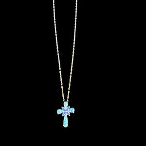 May include: A gold-colored necklace with a cross pendant. The cross is adorned with light blue and purple gemstones. The necklace hangs against a black background.