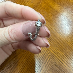 Può includere: Un piercing al naso color argento a forma di cobra. Il cobra ha una testa dettagliata e un corpo curvo. Il piercing al naso è tenuto da una persona.