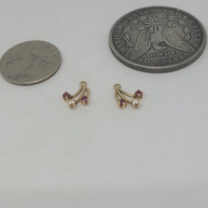 May include: A pair of gold earrings with three red gemstones and a single white gemstone on each earring.