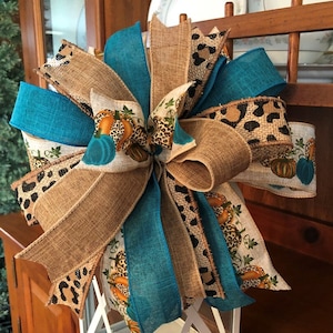 May include: A teal, burlap, and leopard print bow with a pumpkin print ribbon. The bow is tied around a white lantern.