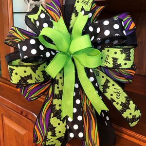 May include: A large Halloween bow with multiple ribbons in black, green, purple, and orange. The bow features polka dots, bat patterns, and the word "eek!". A bright green bow is at the center.
