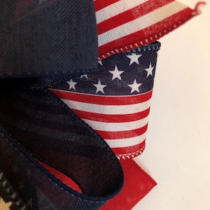 May include: A close-up of a red, white, and blue ribbon with stars and stripes. The ribbon is folded and tied into a bow. The ribbon is perfect for decorating for the Fourth of July or other patriotic holidays.