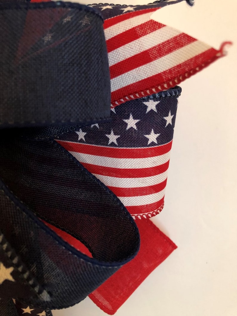 May include: A close-up of a red, white, and blue ribbon with stars and stripes. The ribbon is folded and tied into a bow. The ribbon is perfect for decorating for the Fourth of July or other patriotic holidays.