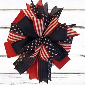 May include: A red, white, and blue patriotic bow with a star-spangled design. The bow is made of ribbon and is perfect for decorating for the Fourth of July or other patriotic holidays.