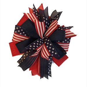 May include: A red, white, and blue patriotic bow with a star-spangled design. The bow is made of fabric and is perfect for decorating for the Fourth of July or other patriotic holidays.