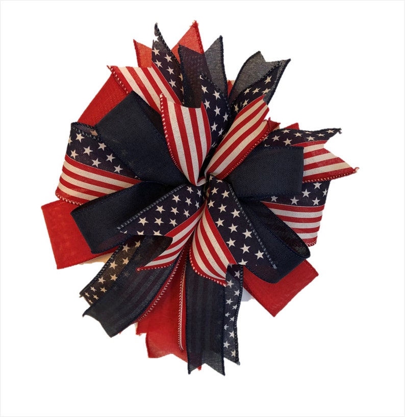 May include: A red, white, and blue patriotic bow with a star-spangled design. The bow is made of fabric and is perfect for decorating for the Fourth of July or other patriotic holidays.