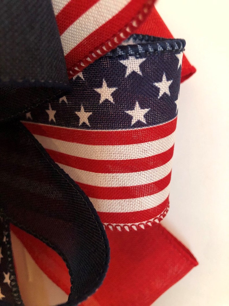 May include: A close-up of a red, white, and blue fabric bow with a star pattern. The bow is made of a woven fabric with a stitched edge.