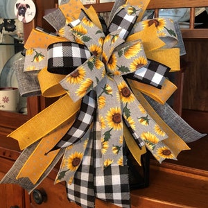 May include: A sunflower themed bow with black and white buffalo check, gray and white sunflower print, and yellow polka dot ribbon. The bow is tied around a black lantern.