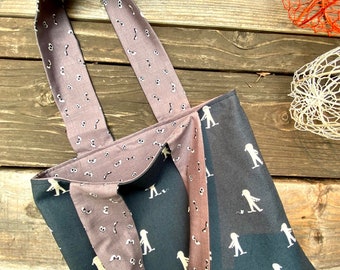 May include: A black tote bag featuring a repeating white pattern of walking figures and small mice. The interior lining and shoulder straps are made of a light brown fabric decorated with a repeating pattern of various pairs of cartoon eyes.