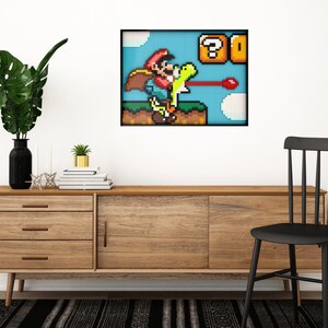 May include: A framed pixel art print of a video game character, Mario, riding a dinosaur-like creature and firing a red projectile. The background is a blue sky with clouds and a question mark block with a coin inside.