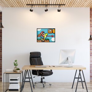 May include: A pixelated image of a video game character, Mario, wearing a red hat and blue overalls, riding a green dinosaur, Yoshi, with a question mark block and a red shell in the background. The image is framed and hanging on a white wall in an office setting.