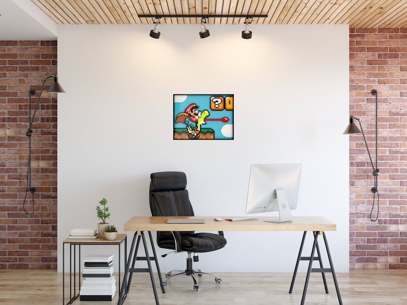 May include: A pixelated image of a video game character, Mario, wearing a red hat and blue overalls, riding a green dinosaur, Yoshi, with a question mark block and a red shell in the background. The image is framed and hanging on a white wall in an office setting.