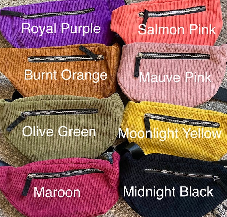 May include: A collection of corduroy fanny packs in various colors, including Royal Purple, Salmon Pink, Burnt Orange, Mauve Pink, Olive Green, Moonlight Yellow, Maroon, and Midnight Black. Each pack features a zippered pocket and a black strap.