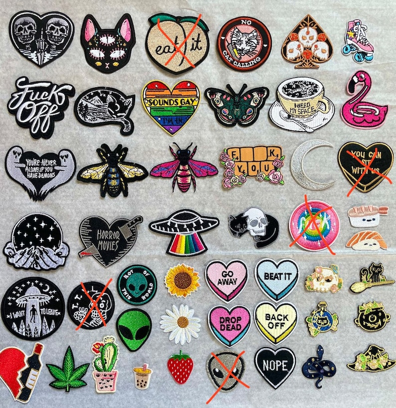 May include: A collection of embroidered iron-on patches featuring various designs, including a cat, a bee, a skull, a UFO, a sunflower, a heart, a moon, a flamingo, and a skull. The patches are colourful and have a variety of themes, including horror, space, and nature.