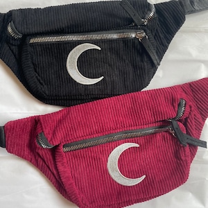 May include: Two corduroy fanny packs with silver crescent moon embroidery. One is black and the other is burgundy.